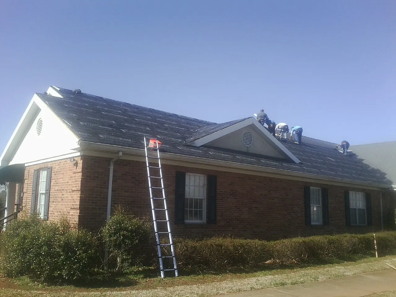 Crew tearing shingles off a brick ranch roof with a ladder set — Emergency Roof Repair work by our crew in Dorset