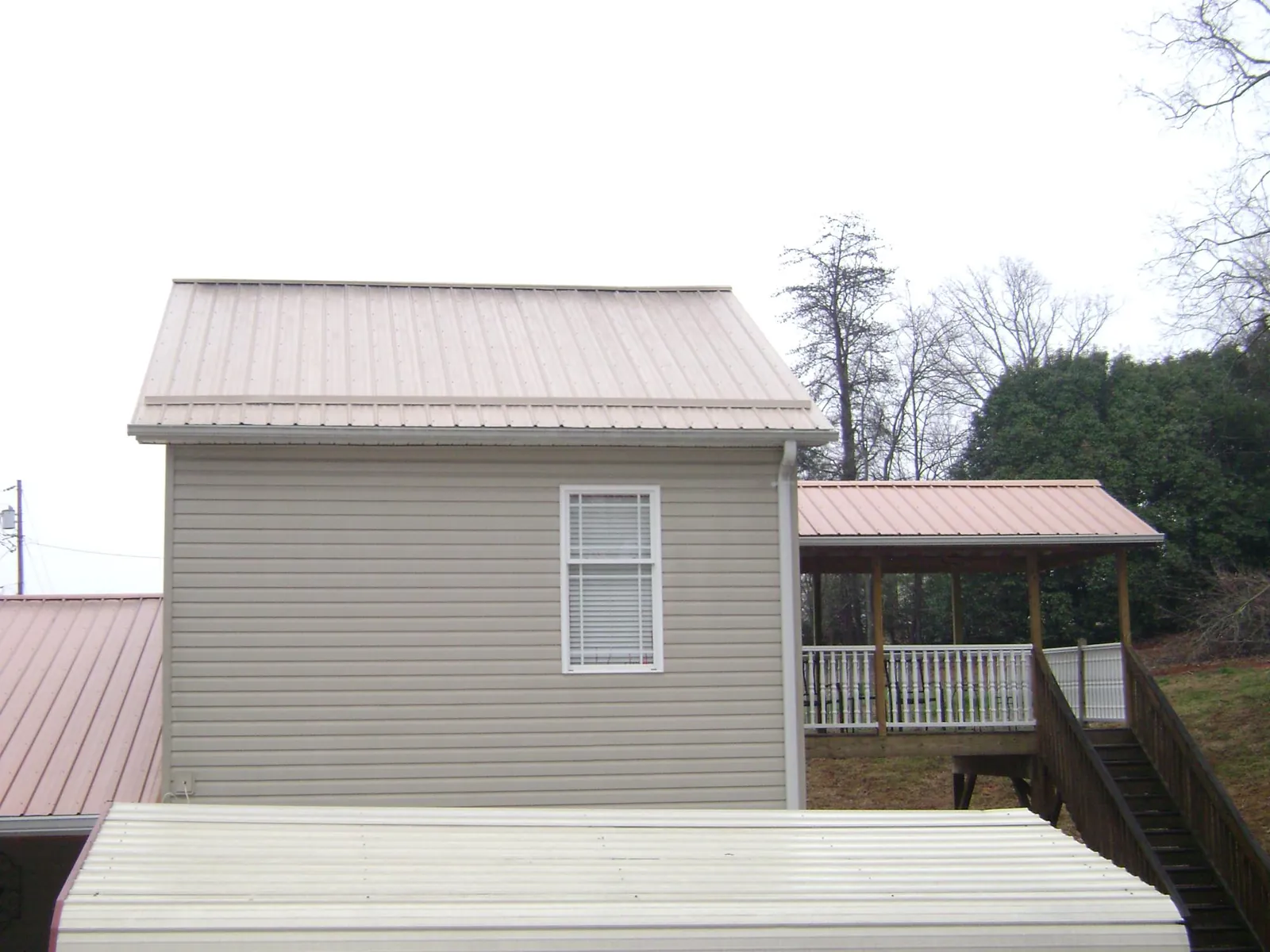 Tan metal roofs on a two story addition and attached porch, from a Roof Replacement job in Dorset